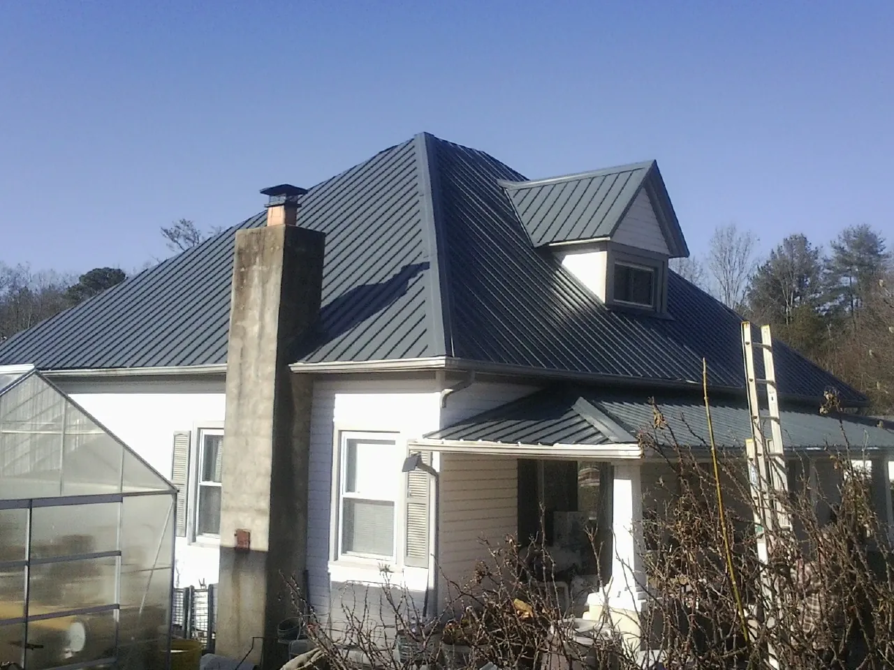Dark blue standing seam metal roof on a white farmhouse with dormer — Slate & Tile Roof Repair by Roofing Brothers in Elmira