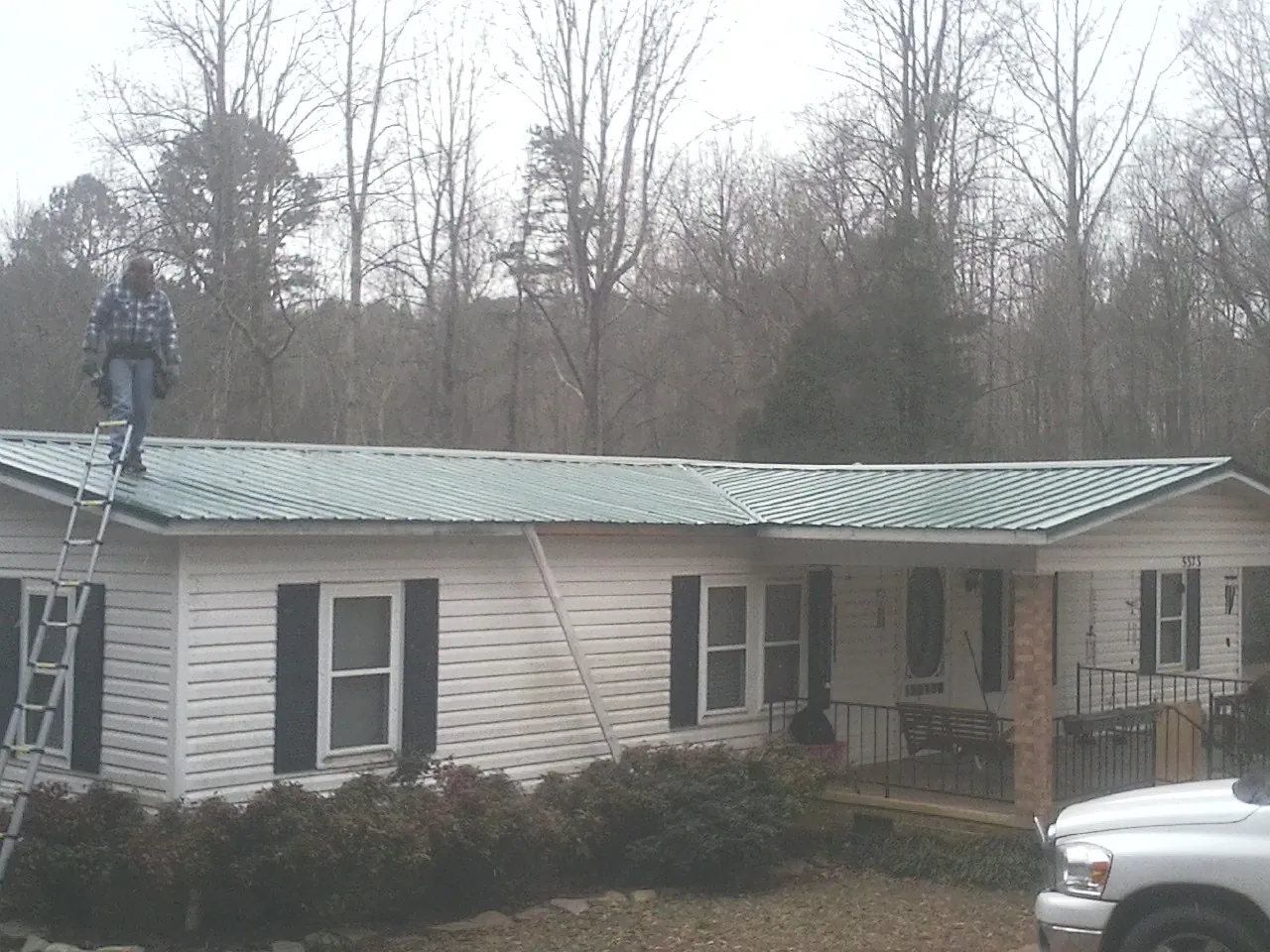 Worker on a ladder beside a new green metal roof on a ranch home in Elmira