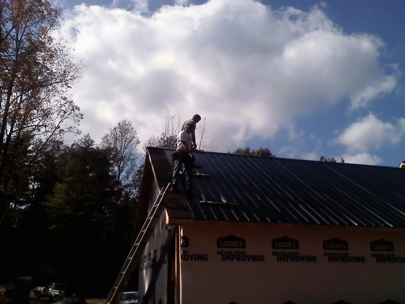 Roofer fastening dark metal panels high against a cloudy sky, from a Roof Inspection job in Elmira