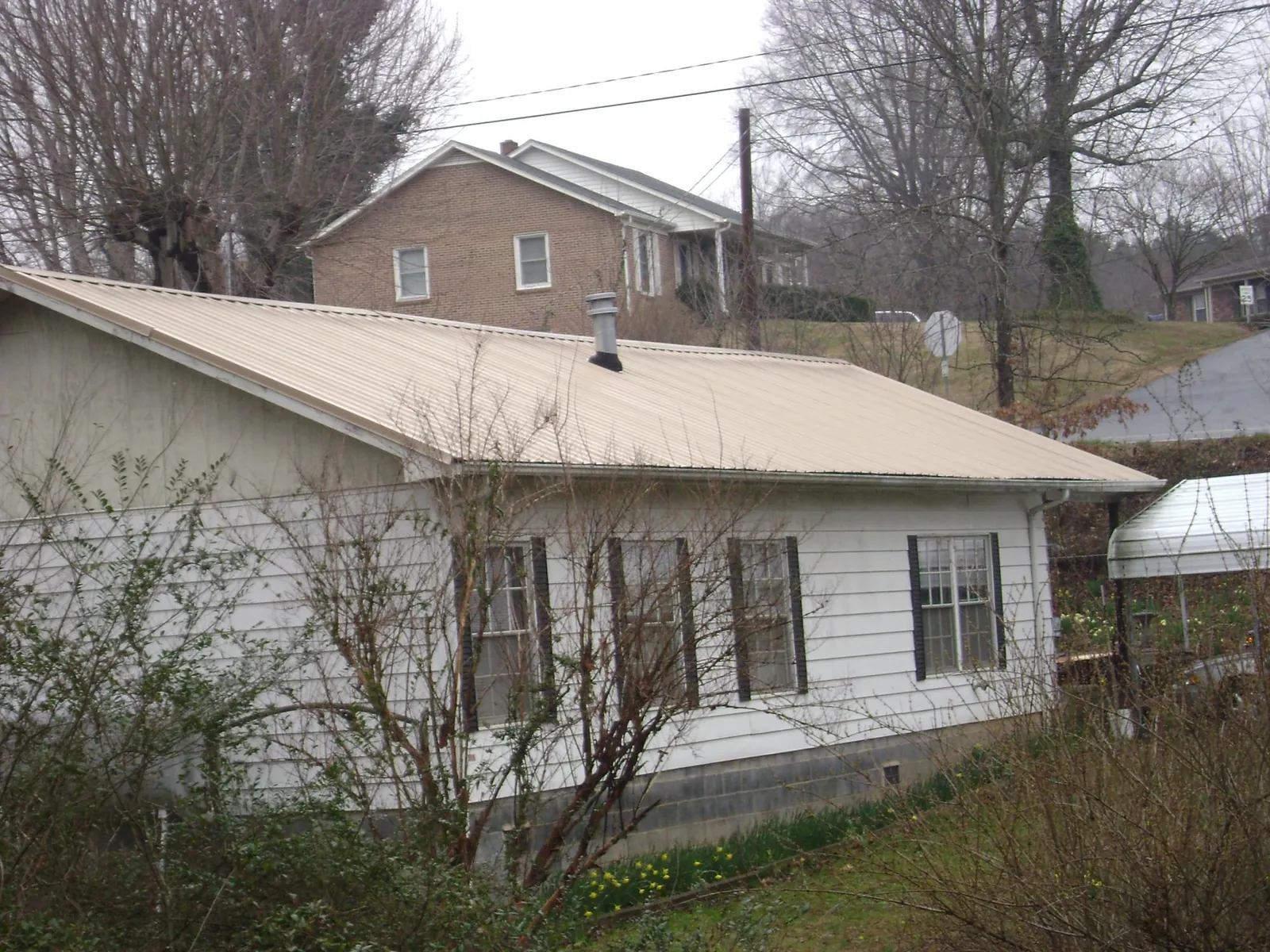 Tan metal roof on a white sided house set into a hillside — Commercial Roofing by Roofing Brothers in Elmira