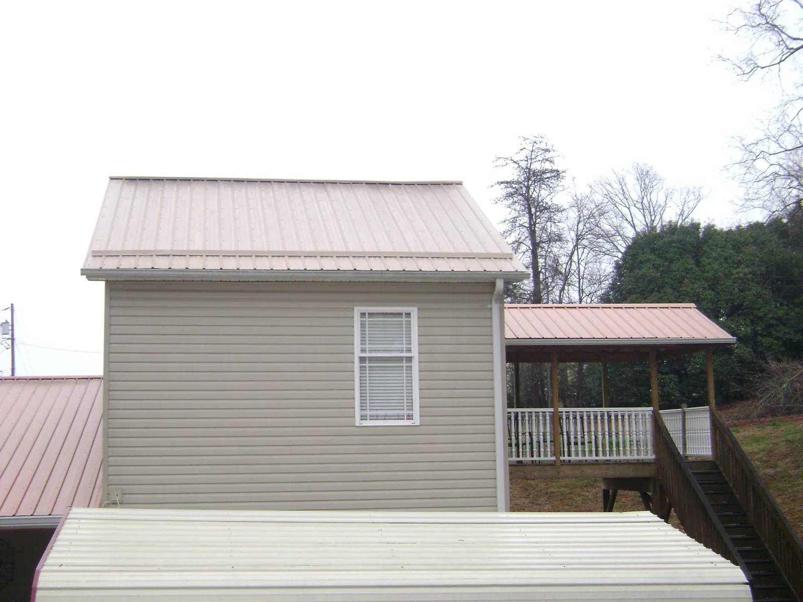 Tan metal roofs on a two story addition and attached porch, from a Roof Replacement job in Elmira